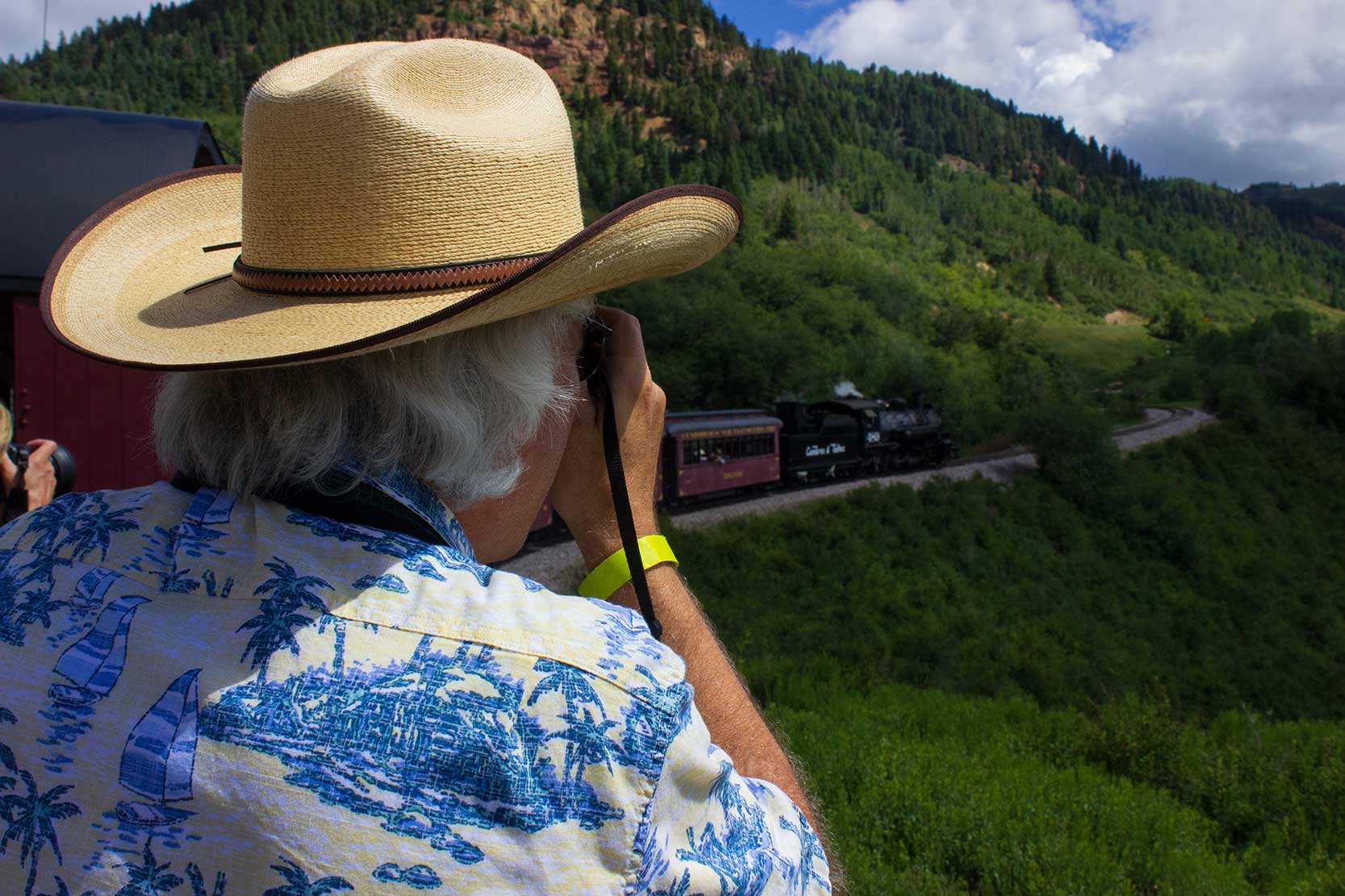 A man takes a photo of a steam locomotive from the gondola car of a train